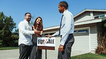 realtor and a couple outside a home with a sold sign